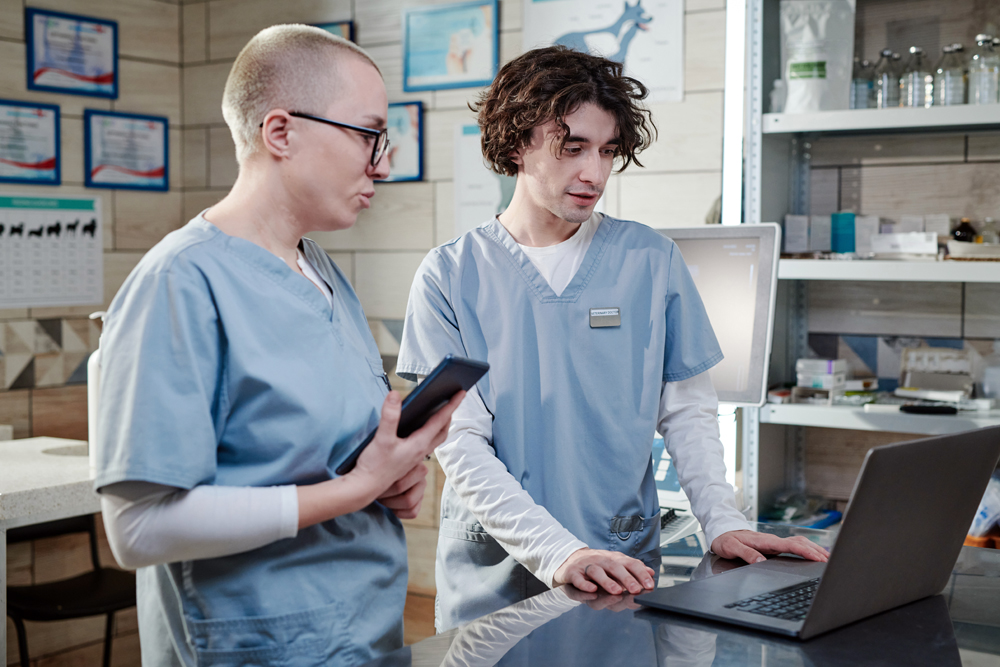 Male,Doctor,Using,Computer,And,Talking,To,His,Colleague,,They