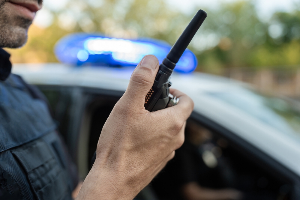 Police,Officer,Is,Holding,A,Walkie,Talkie,Near,A,Patrol